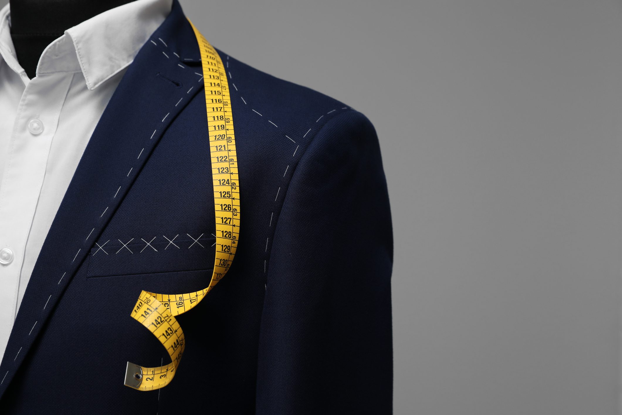 Semi-ready jacket with tailor's measuring tape on mannequin against grey background, closeup. Space for text Semi-ready jacket with tailor's measuring tape on mannequin against grey background, closeup. Space for text